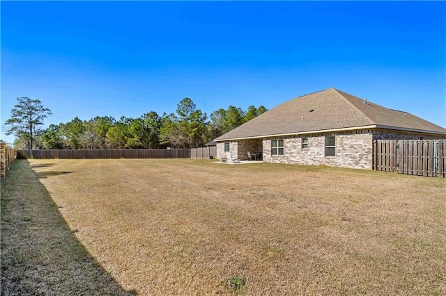 rear view of house featuring brick siding, a fenced backyard, and a yard