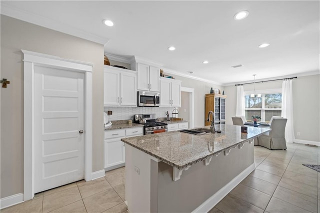 kitchen featuring stainless steel appliances, ornamental molding, white cabinets, an island with sink, and a kitchen breakfast bar