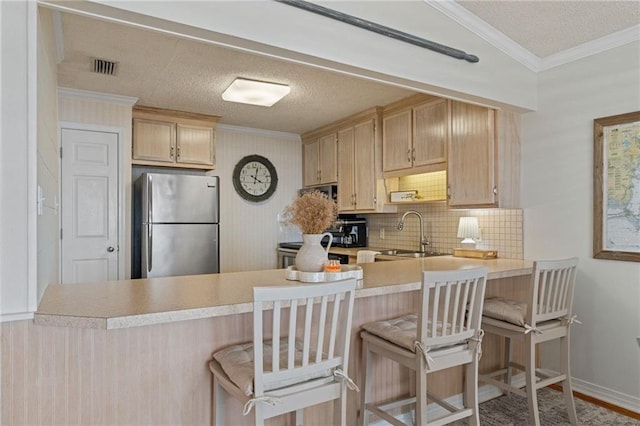 kitchen featuring freestanding refrigerator, a sink, a peninsula, ornamental molding, and light countertops