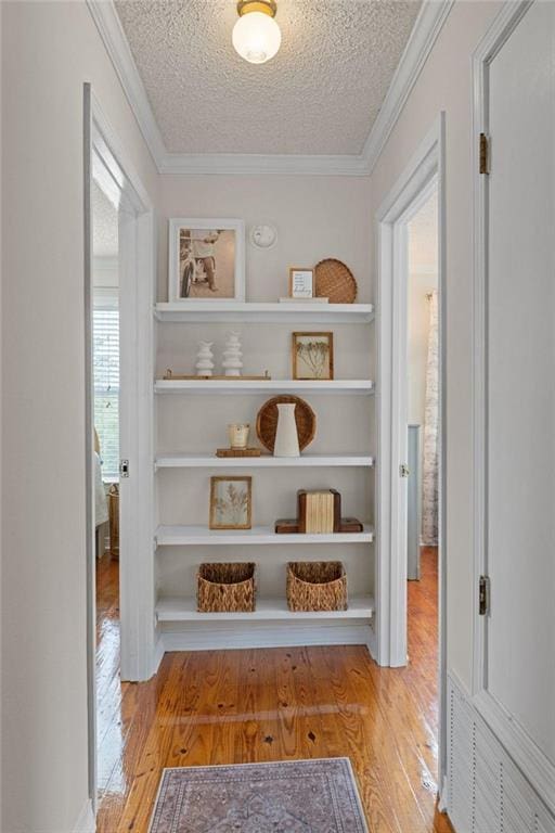 hall with wood finished floors, a textured ceiling, and ornamental molding