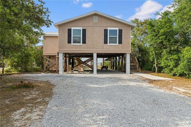 raised beach house with stairs, a carport, driveway, and metal roof
