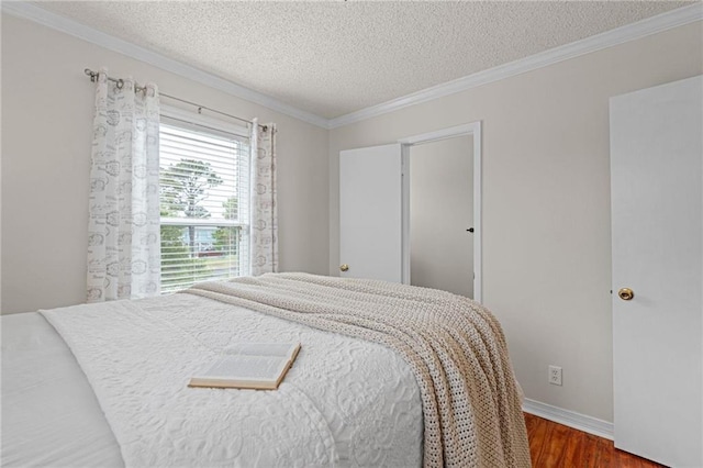 bedroom featuring wood finished floors, a textured ceiling, crown molding, and baseboards