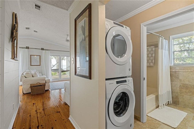 clothes washing area featuring stacked washer and clothes dryer, healthy amount of natural light, a textured ceiling, ornamental molding, and wood-type flooring