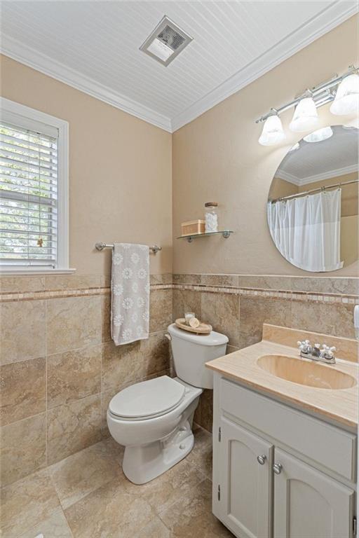 bathroom featuring tile walls, crown molding, vanity, toilet, and a wainscoted wall