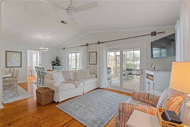 living area featuring ceiling fan, lofted ceiling, light wood-style floors, a textured ceiling, and a chandelier
