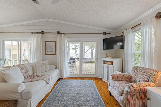 living room featuring lofted ceiling, a textured ceiling, plenty of natural light, light wood-style flooring, and crown molding