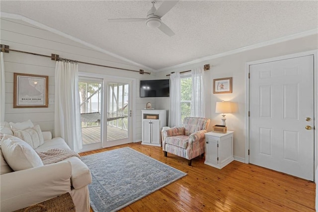 living room with a textured ceiling, vaulted ceiling, a ceiling fan, light wood-type flooring, and crown molding