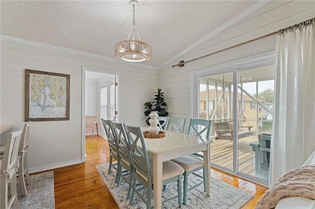 dining room featuring vaulted ceiling, ornamental molding, a textured ceiling, light wood-style flooring, and baseboards
