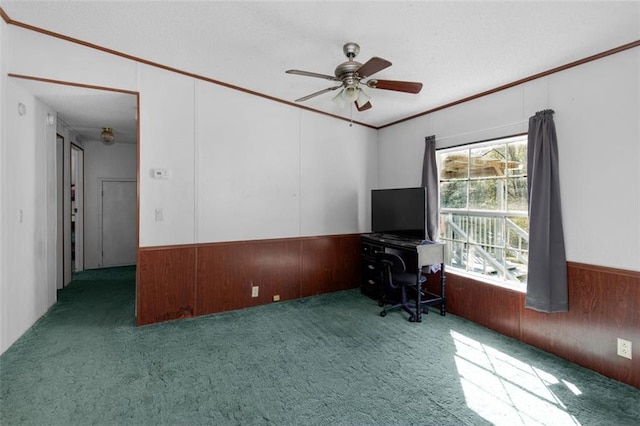 unfurnished office featuring carpet, ornamental molding, a ceiling fan, wainscoting, and wood walls