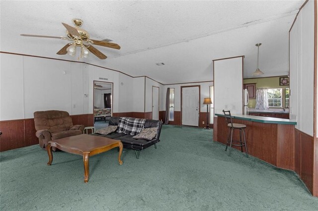 carpeted living room featuring lofted ceiling, ceiling fan, and wooden walls