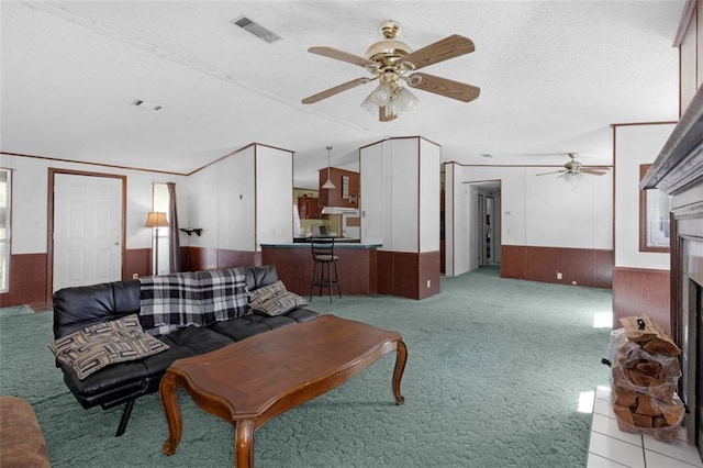 carpeted living room featuring visible vents, a fireplace with raised hearth, a wainscoted wall, ceiling fan, and wood walls