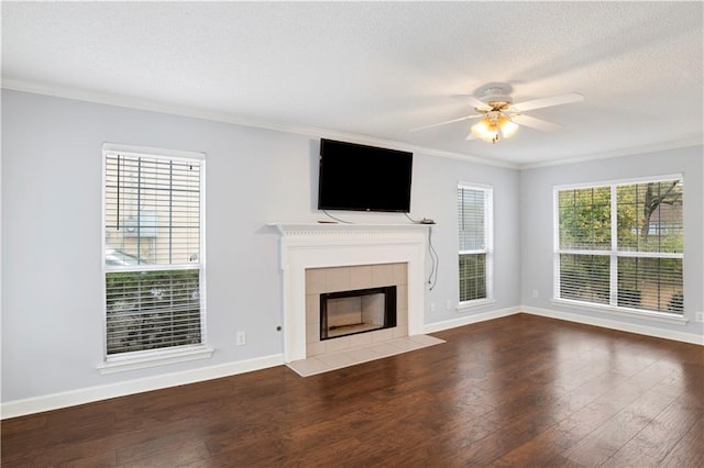 unfurnished living room featuring a tiled fireplace, hardwood / wood-style flooring, ornamental molding, and ceiling fan