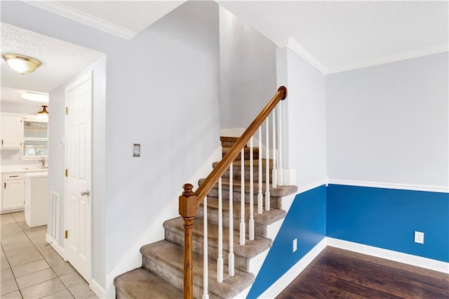 stairs featuring tile patterned flooring, ornamental molding, sink, and a textured ceiling