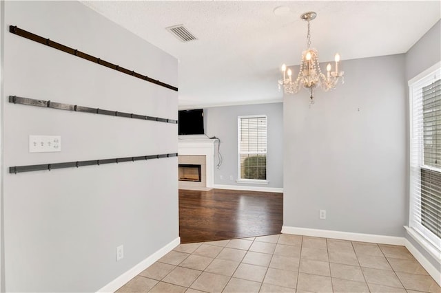 unfurnished dining area featuring a tiled fireplace, light tile patterned floors, and a notable chandelier