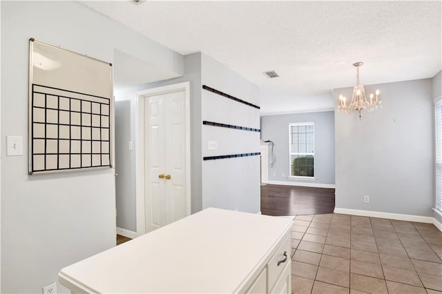 kitchen with a chandelier, a textured ceiling, hanging light fixtures, and white cabinets