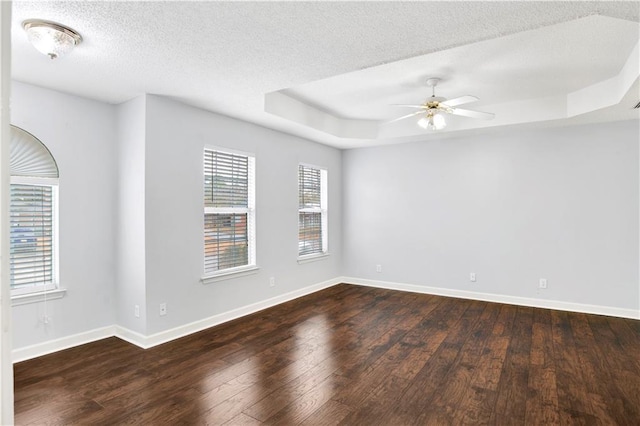 unfurnished room with ceiling fan, dark hardwood / wood-style floors, a textured ceiling, and a tray ceiling