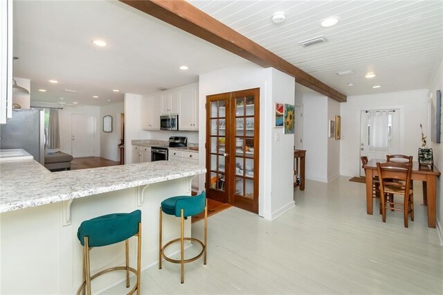 kitchen featuring white cabinetry, light stone counters, kitchen peninsula, beamed ceiling, and stainless steel appliances