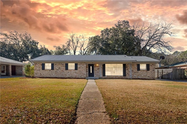 ranch-style house featuring metal roof, a lawn, and brick siding