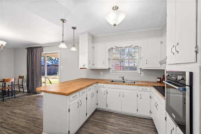 kitchen featuring a peninsula, a sink, stainless steel oven, dark wood finished floors, and crown molding