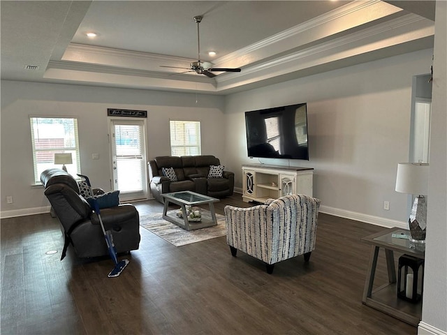 living room with a tray ceiling, dark wood-type flooring, ornamental molding, and ceiling fan