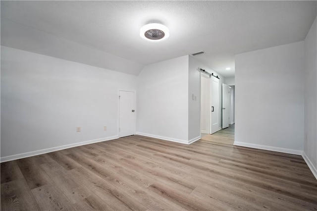 709 Oak Field Dr, Mobile, AL 36609 - empty room featuring a barn door, wood finished floors, baseboards, and vaulted ceiling