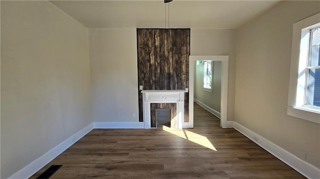 unfurnished living room featuring a fireplace, a healthy amount of sunlight, and dark hardwood / wood-style floors