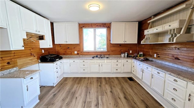 kitchen featuring light stone counters, wooden walls, light hardwood / wood-style floors, white cabinetry, and sink