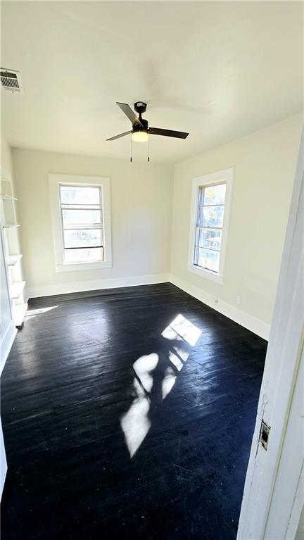 spare room with ceiling fan, a wealth of natural light, and dark hardwood / wood-style floors