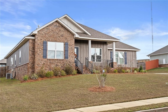 view of front facade with central air condition unit, brick siding, board and batten siding, and a front yard