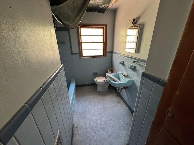 full bathroom featuring a sink, tile walls, toilet, and wainscoting