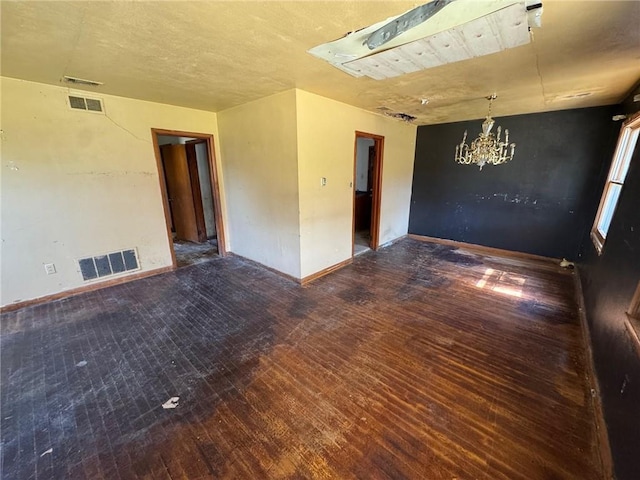 empty room featuring a chandelier, visible vents, baseboards, and wood-type flooring