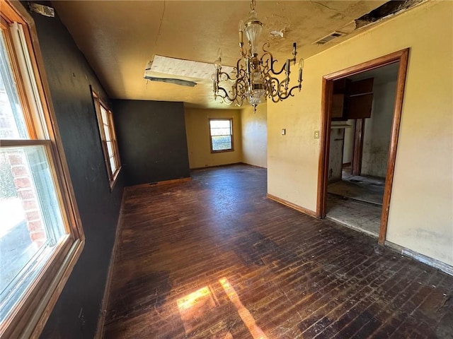 unfurnished dining area with hardwood / wood-style floors, an inviting chandelier, baseboards, and visible vents