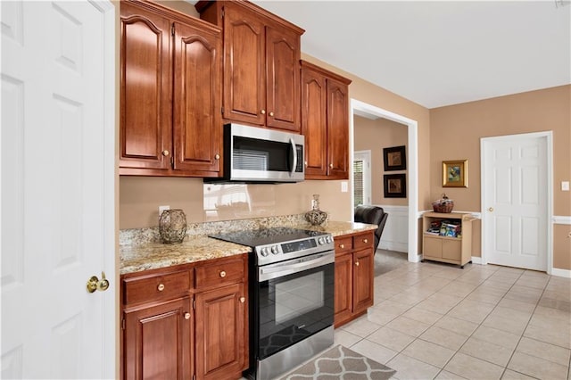 kitchen with light stone counters, light tile patterned floors, brown cabinets, and stainless steel appliances