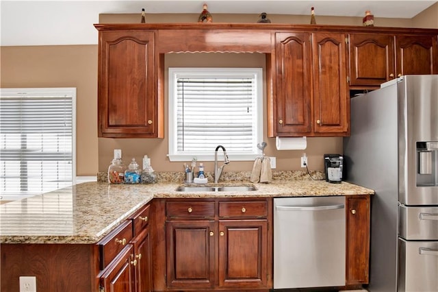 kitchen featuring stainless steel appliances, light stone counters, plenty of natural light, and a sink