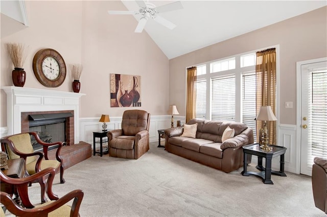 living area with ceiling fan, light colored carpet, a fireplace, high vaulted ceiling, and a wainscoted wall