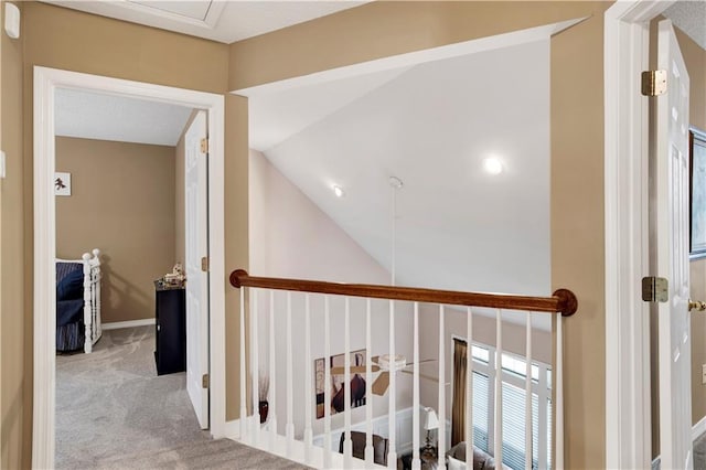 hallway with carpet floors, baseboards, lofted ceiling, and an upstairs landing