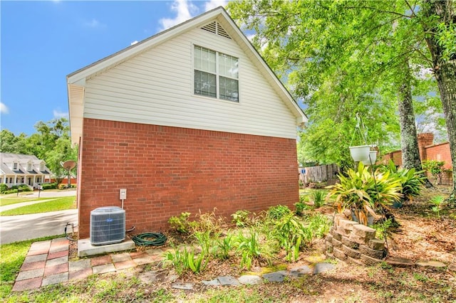 view of side of property with central air condition unit, brick siding, and fence