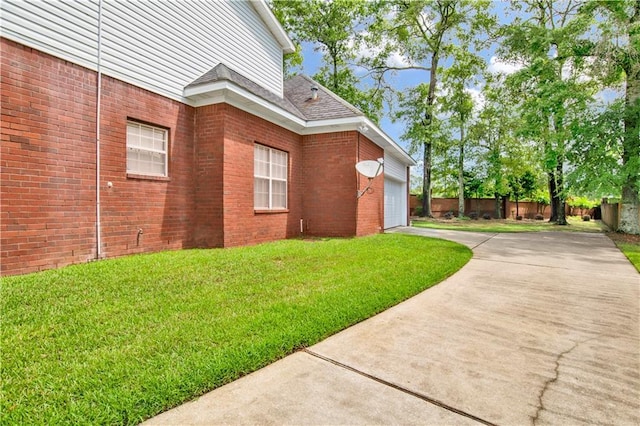 view of side of property featuring fence, driveway, brick siding, an attached garage, and a yard