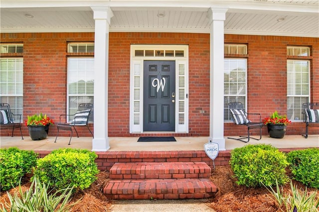 view of exterior entry featuring covered porch and brick siding