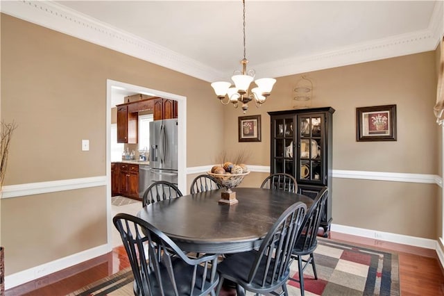 dining space with an inviting chandelier, baseboards, crown molding, and light wood finished floors