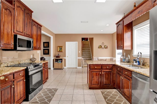 kitchen featuring light stone countertops, appliances with stainless steel finishes, a sink, a peninsula, and light tile patterned floors