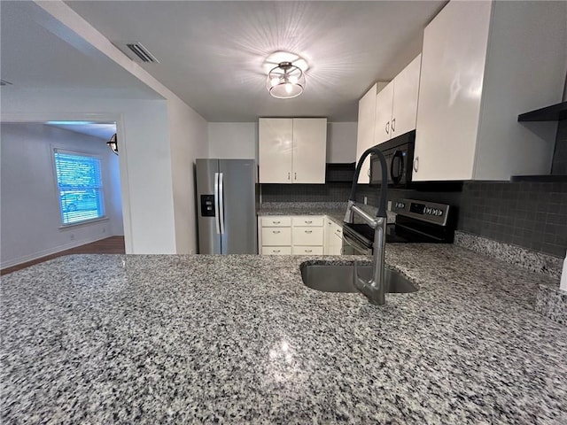 kitchen with decorative backsplash, white cabinetry, stainless steel appliances, and dark stone counters