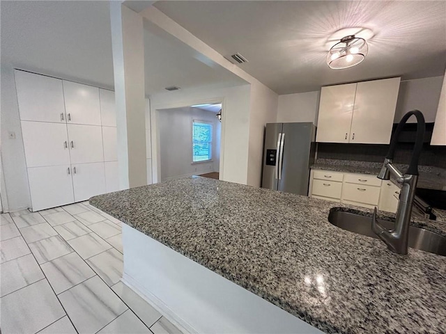 kitchen with dark stone counters, sink, kitchen peninsula, and stainless steel fridge