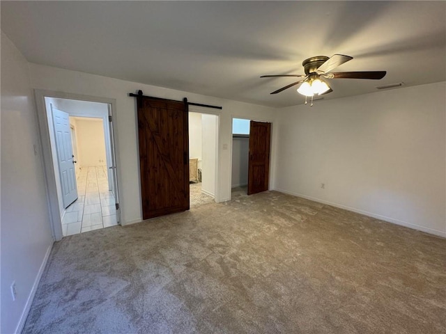 unfurnished bedroom featuring a barn door, light colored carpet, and ceiling fan