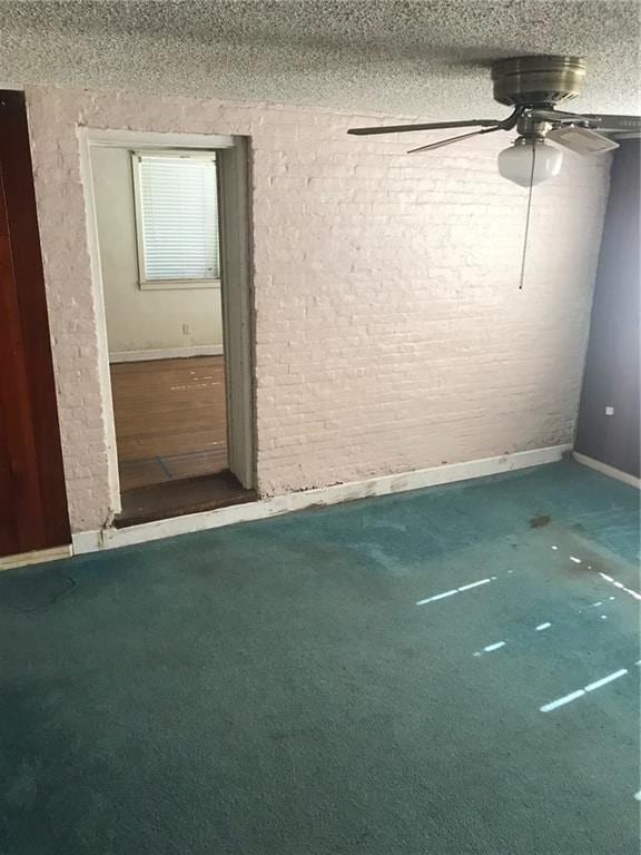 carpeted spare room with ceiling fan, brick wall, and a textured ceiling