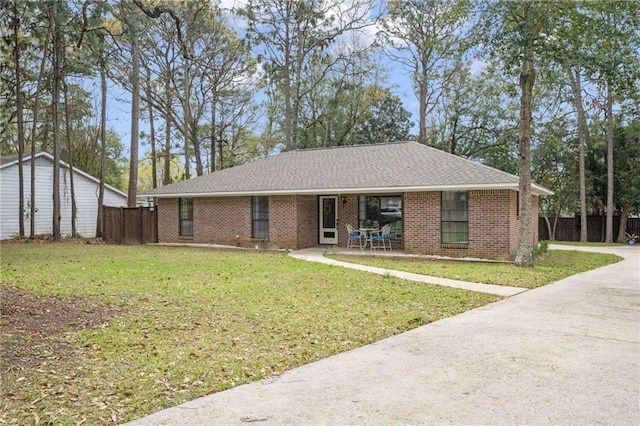 ranch-style home with a shingled roof, a front yard, brick siding, and fence