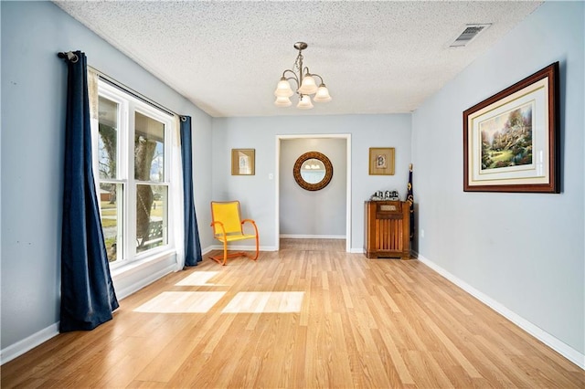 unfurnished room with a textured ceiling, light hardwood / wood-style flooring, and a notable chandelier