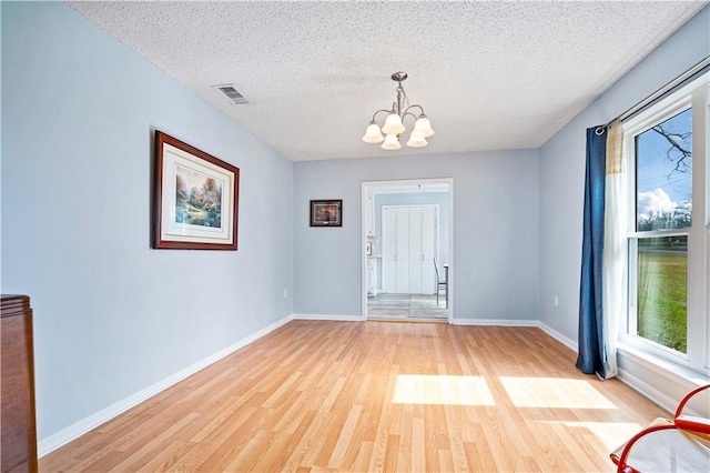 foyer entrance with a notable chandelier, a textured ceiling, and light wood-type flooring