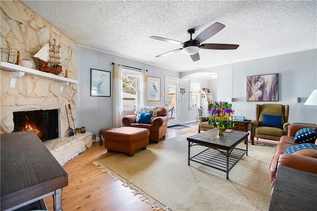 living room featuring ceiling fan, a fireplace, hardwood / wood-style floors, and a textured ceiling