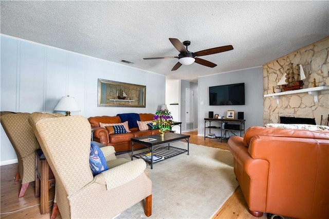 living room featuring ceiling fan, a fireplace, light hardwood / wood-style floors, and a textured ceiling